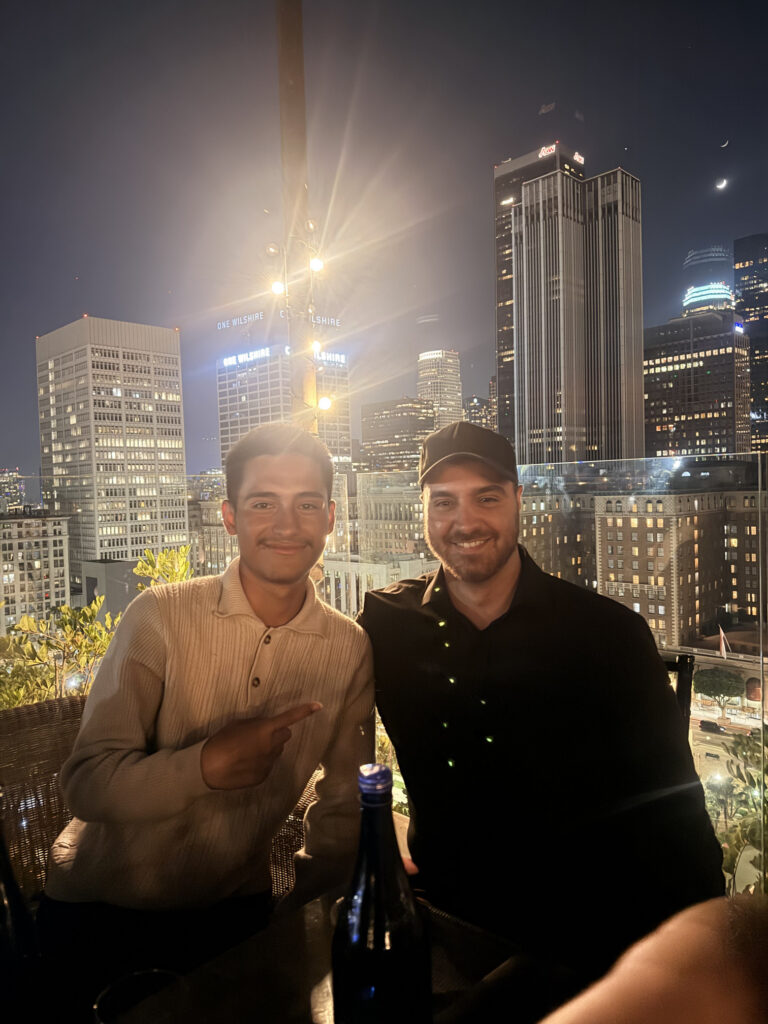 Two professionals networking on a rooftop overlooking the Los Angeles skyline at night